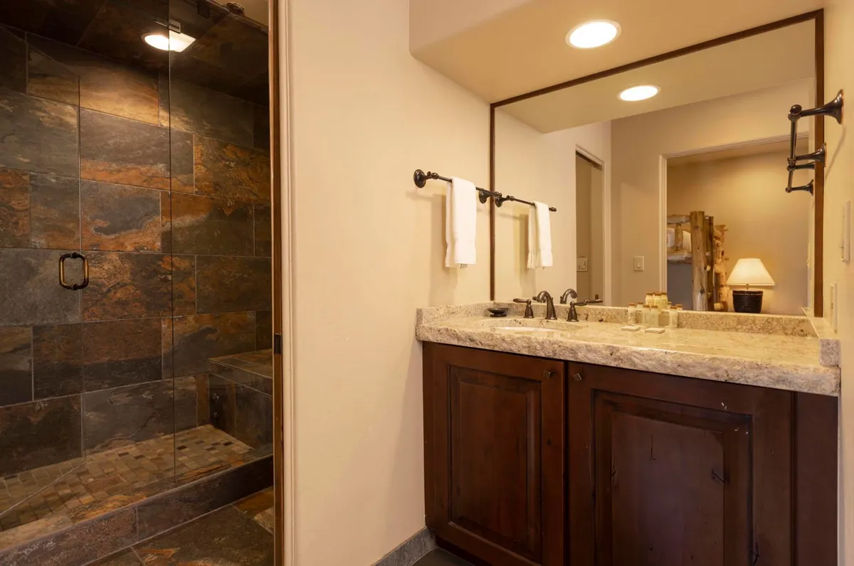 This tranquil bathroom scene displays a shower area, a vanity with sink, and a mirror. It evokes feelings of relaxation, ideal for refreshing morning starts or unwinding at the end of the day.
