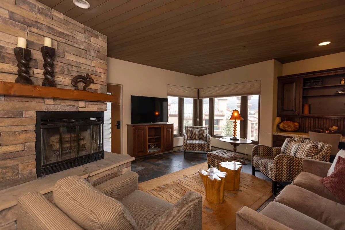 A cozy, inviting living area with a crackling fireplace, plush seating, and expansive windows offering stunning mountain views—perfect for relaxing after a day on the slopes or gathering with loved ones.