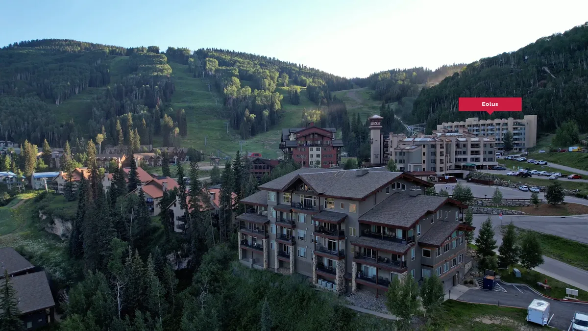 This image captures a wide view of the mountain landscape surrounding Purgatory Resort, featuring wooded areas, residential buildings, and visible ski resort facilities. The scene conveys immediate access to outdoor adventure, with the resort nestled at the base of dramatic peaks and trails.