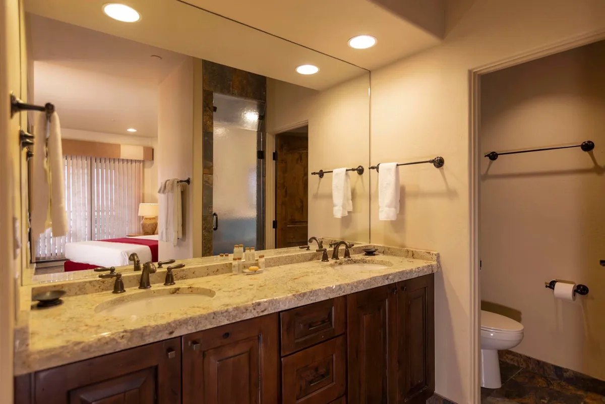 A calming bathroom interior with a double sink vanity, granite countertops, a large mirror, and towel racks. The space is ideal for shared morning routines or evening wind-downs, emphasizing both functionality and relaxation.