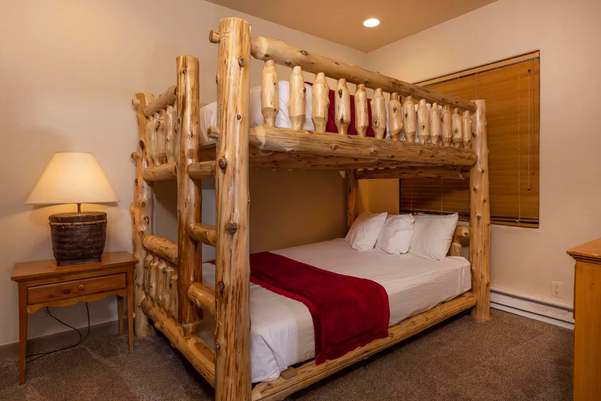 The image captures a playful yet comfortable bedroom with a bunk bed, a table lamp, and a red throw blanket. The space feels inviting for both sleep and bedtime storytelling, appealing to families and children seeking comfort and fun.