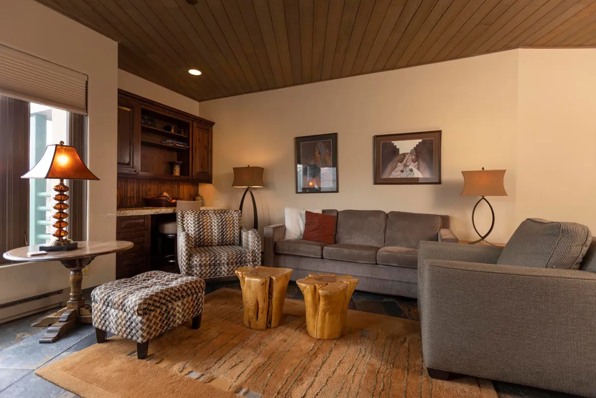 A welcoming interior living space featuring a comfortable sofa, wooden stools, a cozy lamp, and vibrant artwork. The arrangement invites relaxing, socializing, and gathering after a day of activities.