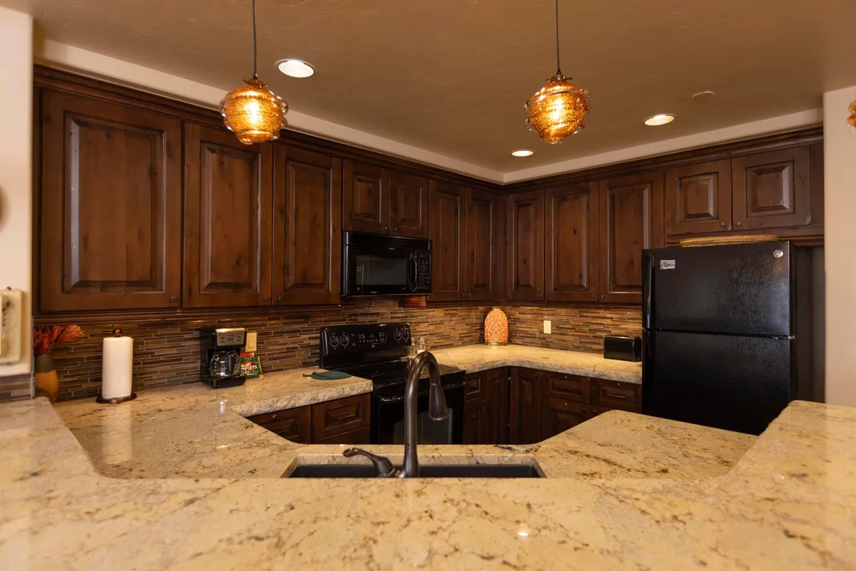 A warmly lit kitchen featuring granite countertops, wooden cabinets, pendant lights, and modern appliances. The layout is open and inviting, with ample space for preparing meals and gathering with family.