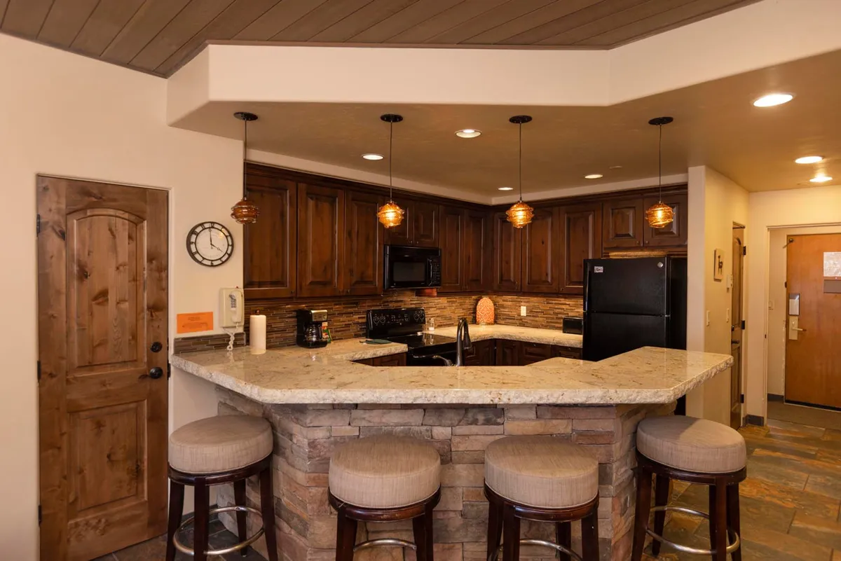 A close-up view of a kitchen bar with granite countertops, wood cabinetry, and stylish pendant lighting. Bar stools are positioned at the counter, creating a spot for casual dining or chatting with the cook.