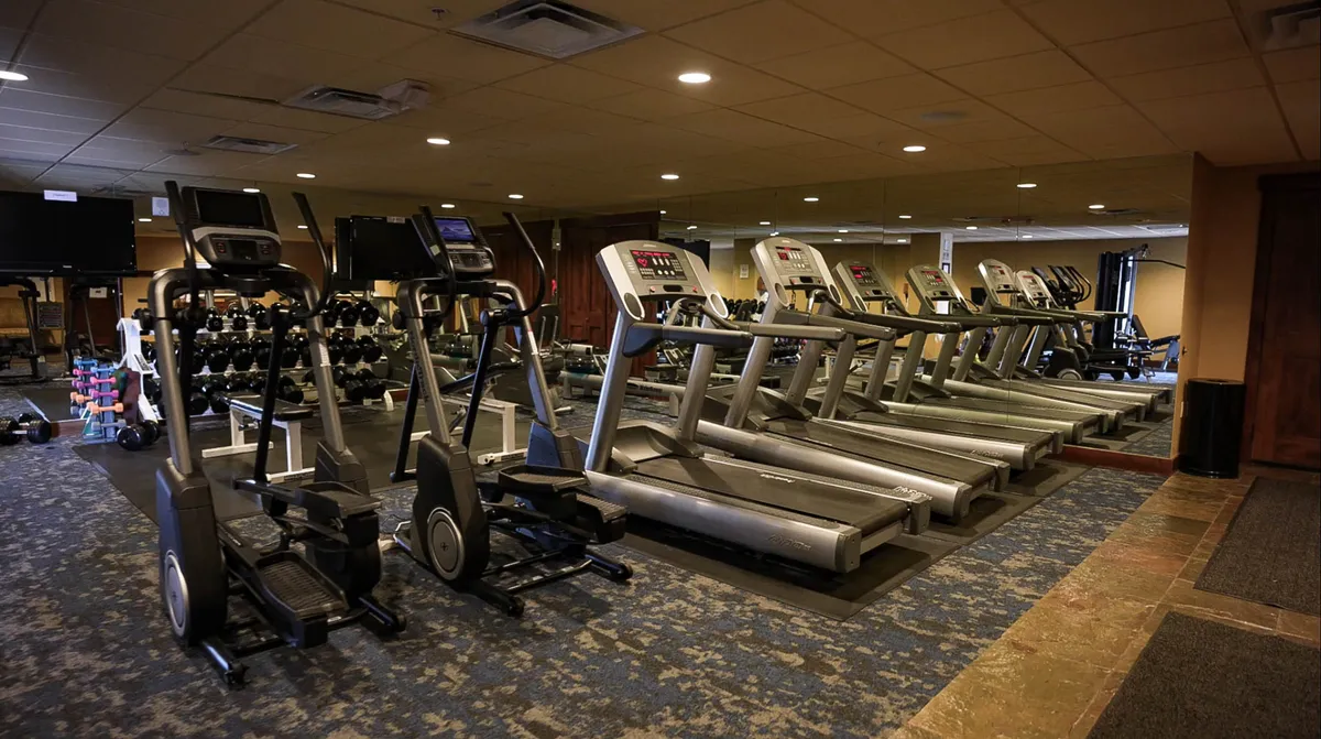 A modern fitness facility featuring treadmills, ellipticals, weightlifting equipment, and mirrors. The space is bright and inviting, with a motivational atmosphere that encourages guests to stay active.
